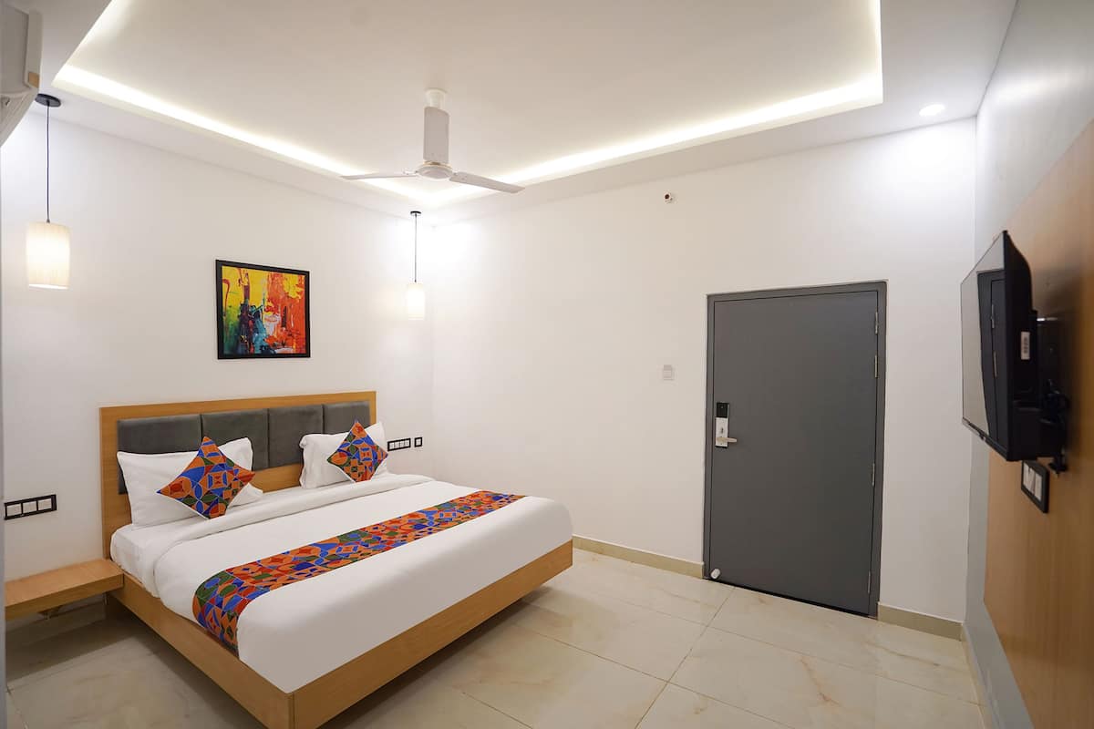 A modern hotel room with a bed, a ceiling fan, a door, and a mounted TV.