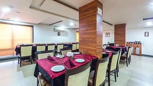A dining area with tables set for meals, chairs, and a wooden pillar with a sign. - FabHotel Skylark Inn (Nashik)
