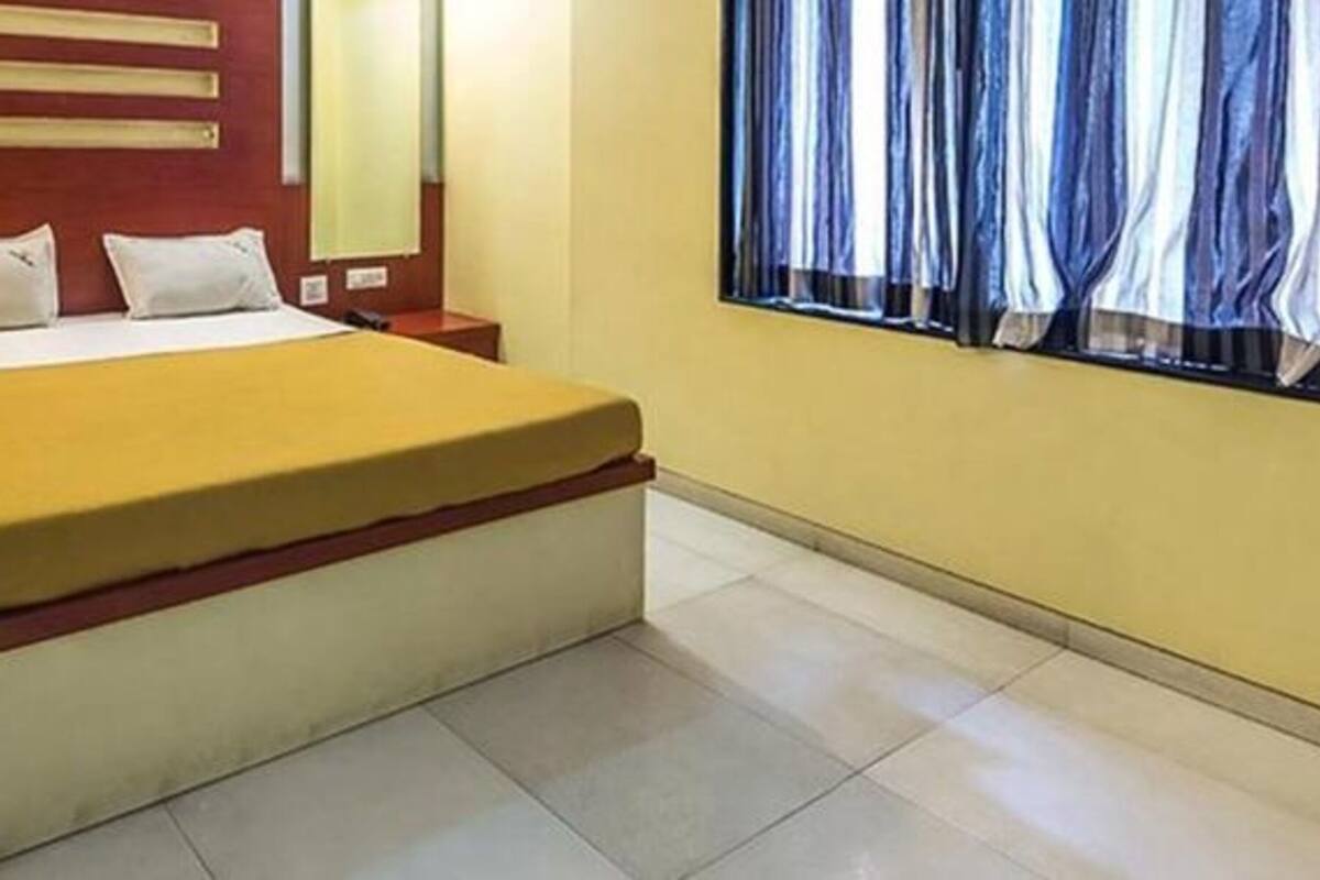 Une chambre d’hôtel avec un lit, une table de chevet, un miroir et une fenêtre avec des rideaux.