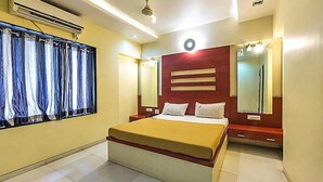 A hotel room with a bed, a window with curtains, a mirror, and a wall-mounted air conditioning unit. - FabHotel Skylark Inn (Nashik)