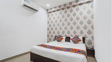 A hotel room with a bed, a nightstand, an air conditioning unit, and patterned wallpaper.