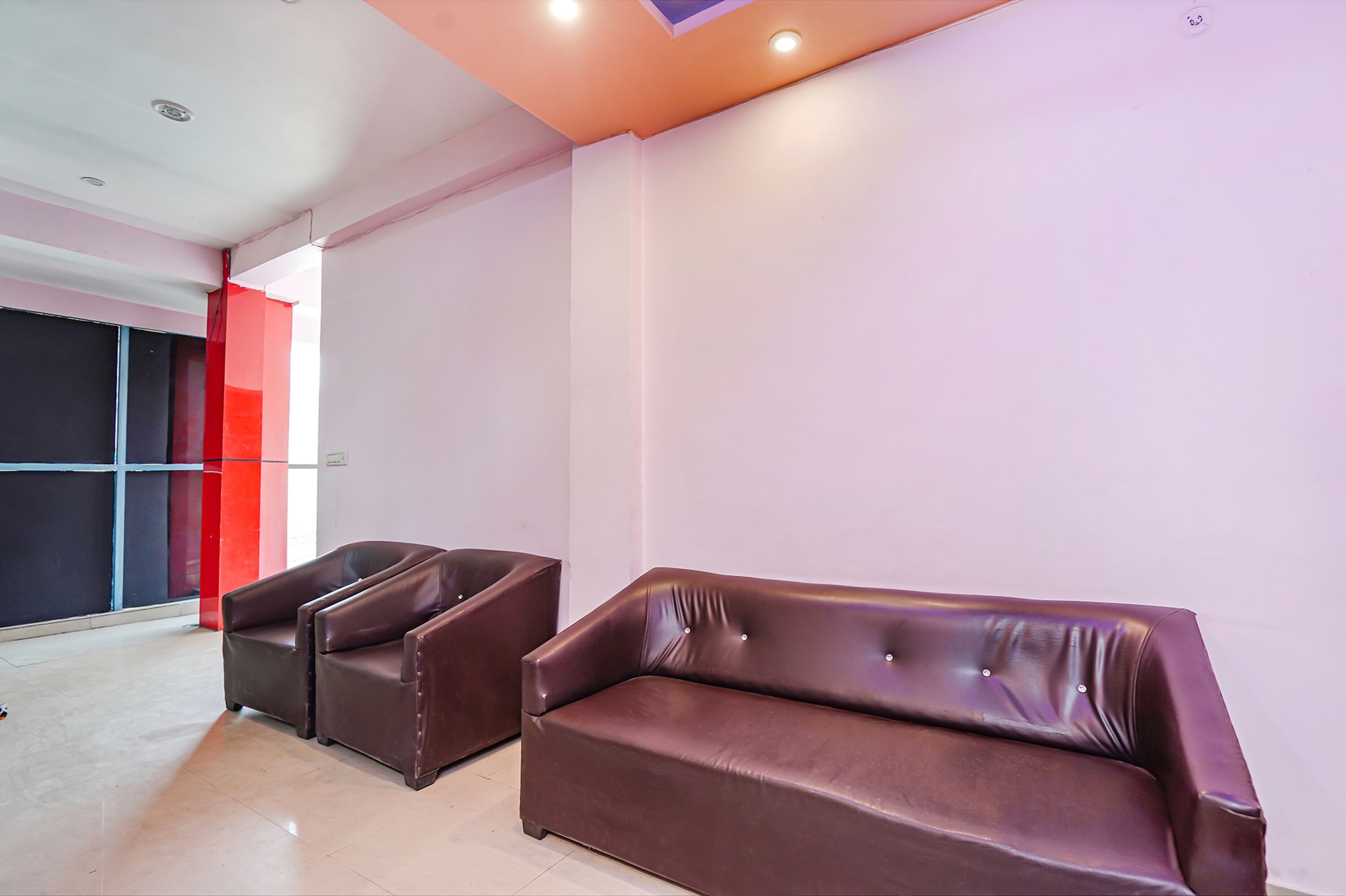 A modern interior with a brown leather sofa and armchairs, a white wall, and a red accent wall.
