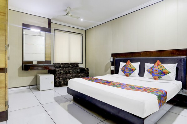 A hotel room with a large bed, a small desk, a mirror, and a ceiling fan.