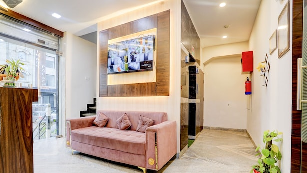 A modern lobby with a pink sofa, a mounted TV, and a red fire extinguisher. - FabHotel SMR (Agra)