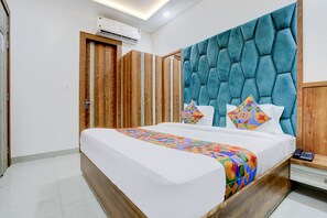 A modern bedroom with a large bed, wooden wardrobe, and a teal upholstered headboard. - FabHotel SMR (Agra)