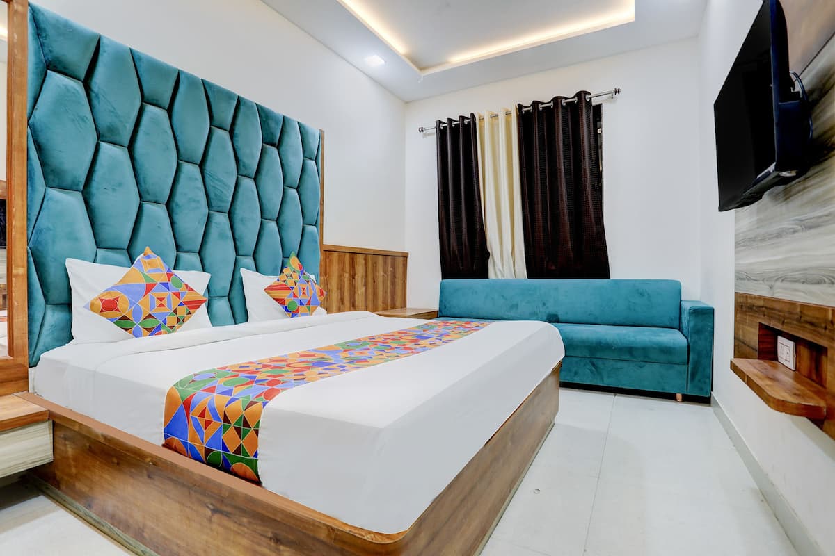 A modern hotel room with a large bed, a blue sofa, and a flat-screen TV mounted on the wall.