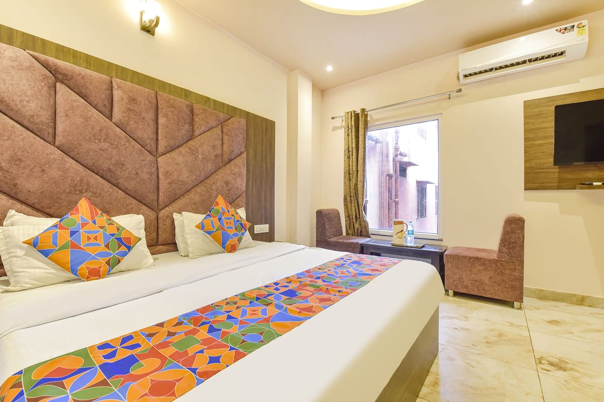 Habitación de hotel con una cama grande, cabecera con diseños geométricos, televisor montado en la pared y una ventana con cortinas.