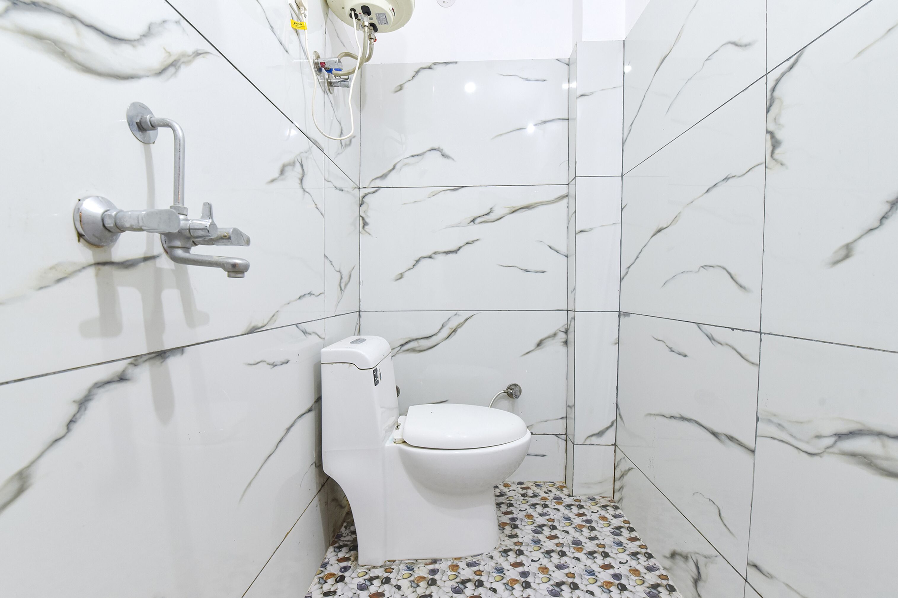 A bathroom with a toilet, a shower, and a marble-patterned floor.