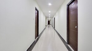 A long, narrow hallway with white walls and a tiled floor, leading to a door at the end. - FabExpress Royal Prime Suits (Hyderabad)