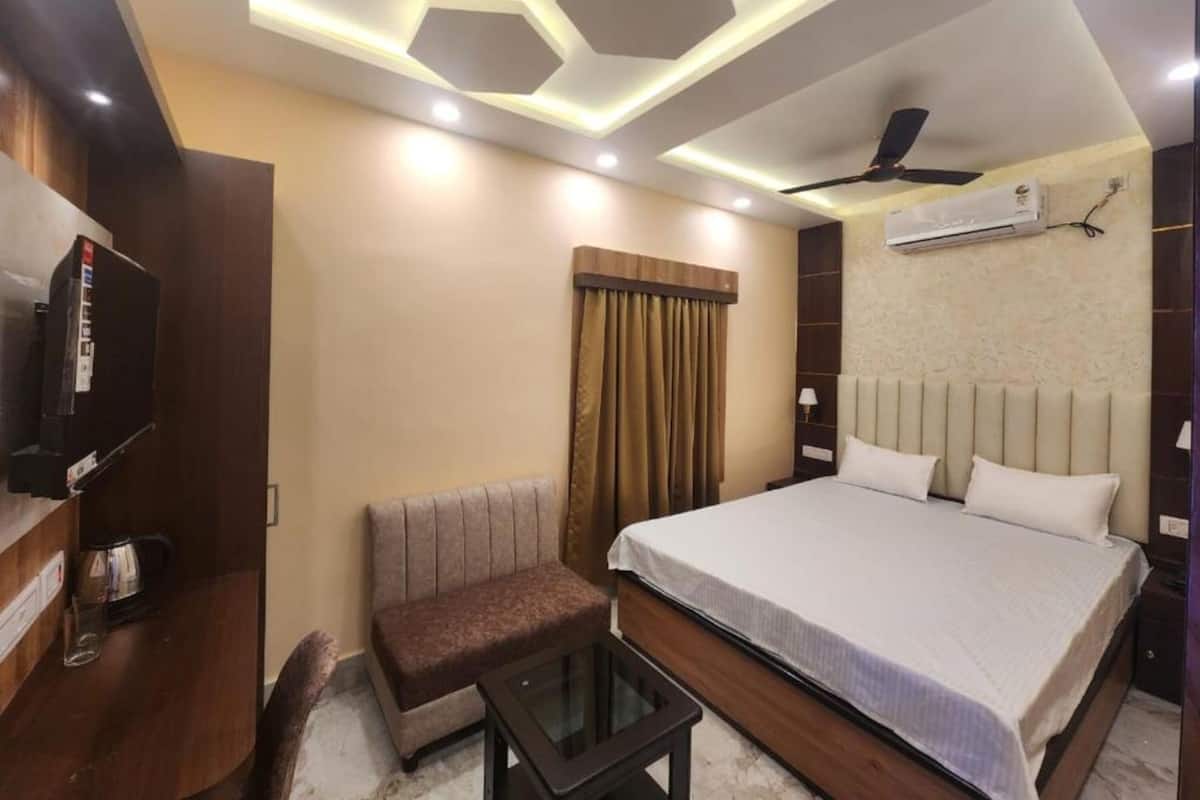 A modern hotel room with a bed, a TV, a sofa, a small table, and a ceiling fan.