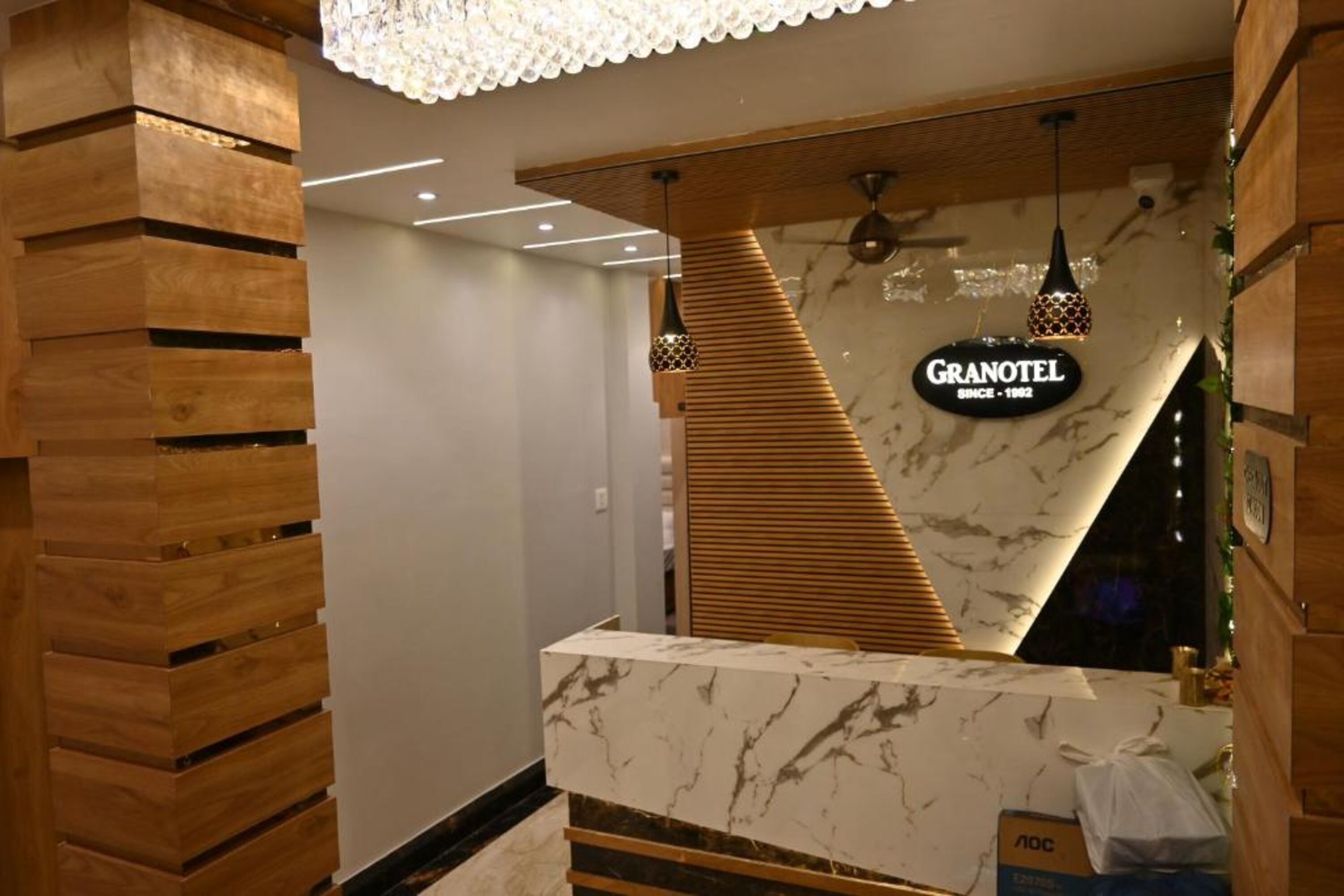 A hotel reception area with a marble counter, wooden slatted wall, and a chandelier.