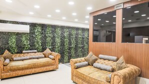 A reception area with two sofas, a wooden reception desk, and a wall with a green leafy pattern. - FabHotel Prime Simran (Rajkot)