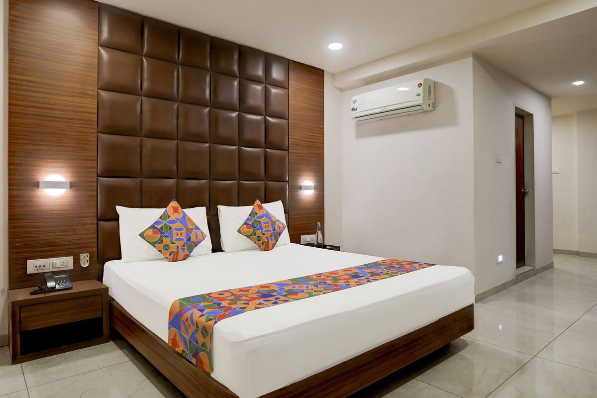 Une chambre d’hôtel avec un grand lit, une tête de lit en bois, deux tables de chevet, un appareil de climatisation et une porte.