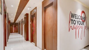 A hotel corridor with wooden doors, a welcome sign, and a clean tiled floor. - FabHotel Prime Simran (Rajkot)