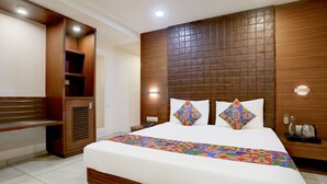 A hotel room with a large bed, wooden headboard, built-in wardrobe, bedside table, and a bench. - FabHotel Prime Simran (Rajkot)