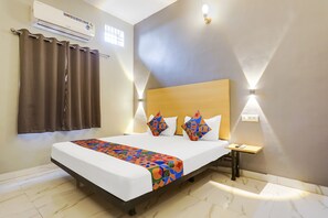 Habitació d'hotel amb un llit, una tauleta de nit, aire condicionat i una finestra amb cortines.