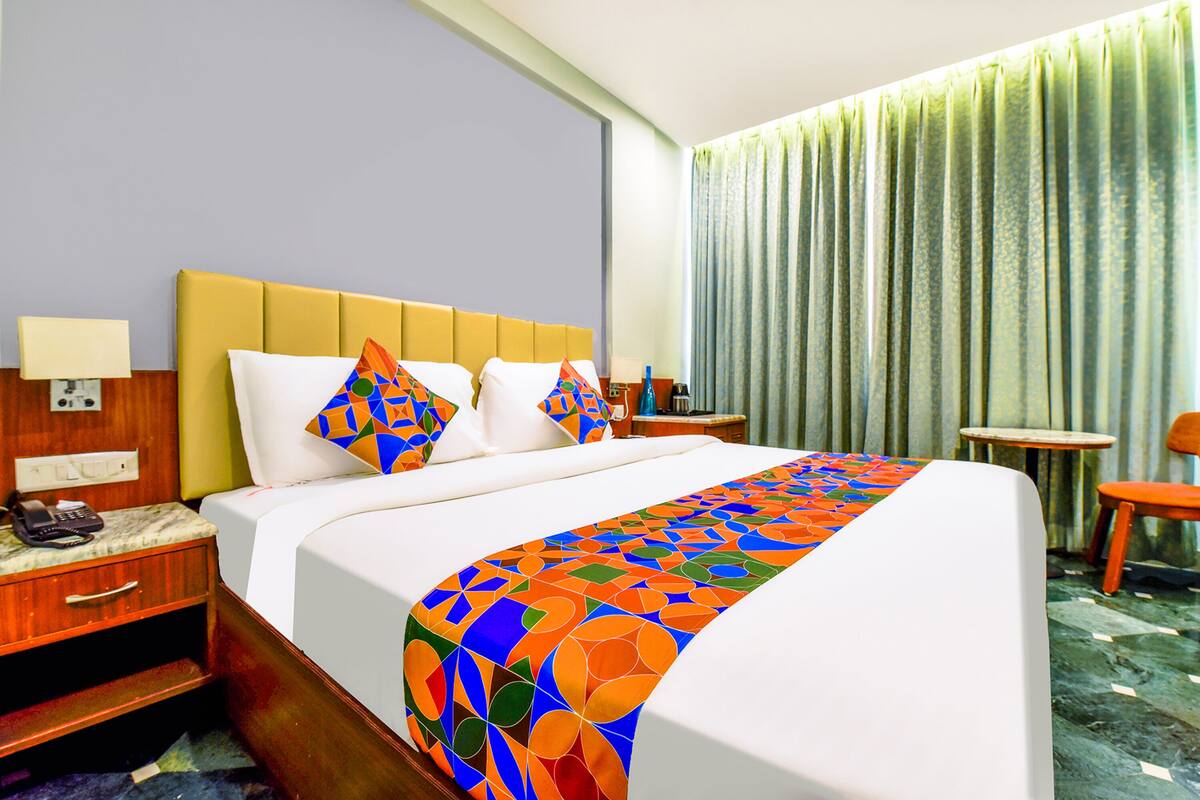A hotel room with a bed, a nightstand, a lamp, a telephone, a table, and a chair.