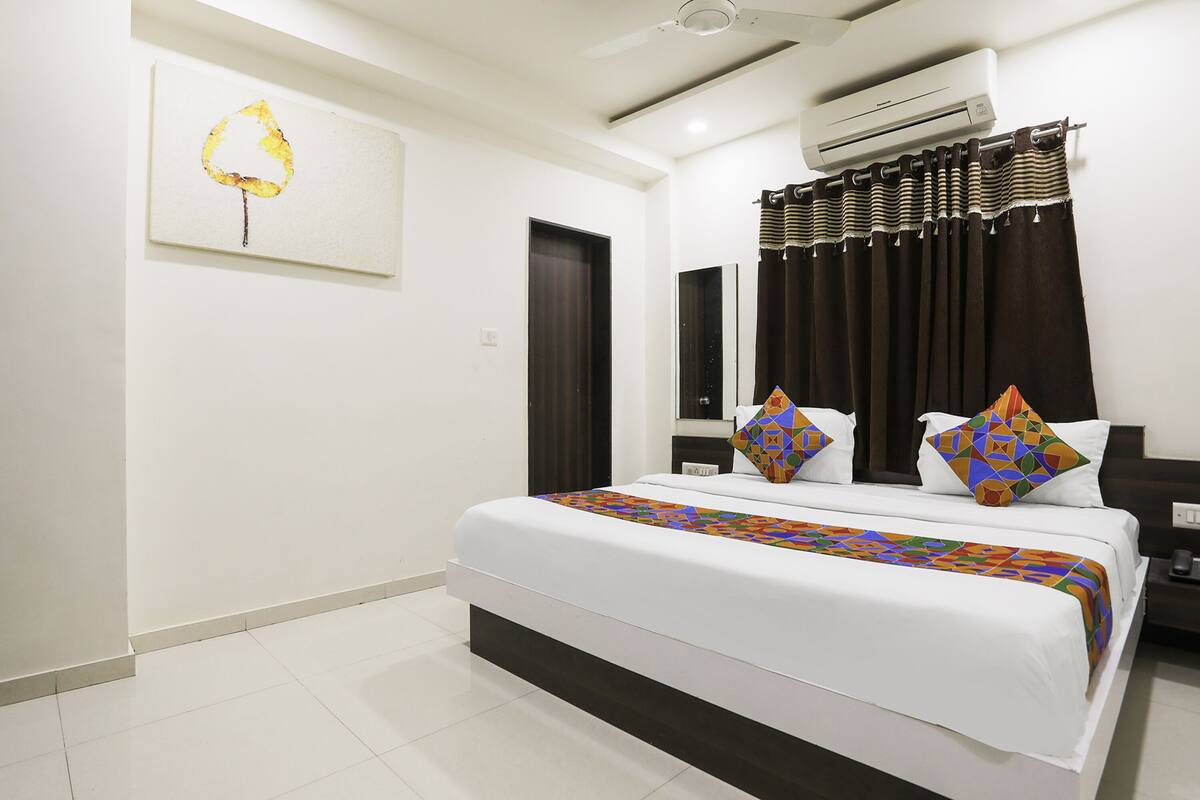Una habitación de hotel con una cama grande, un ventilador de techo, un equipo de aire acondicionado y una cortina oscura.