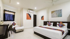 A hotel room with a bed, a desk, and a chair. There is a window with curtains, a ceiling fan, and artwork on the walls. - FabHotel SK (Rajkot)