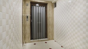 A hotel elevator with a digital display, marble walls, and a tiled floor. - FabHotel SK (Rajkot)