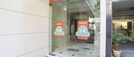A hotel entrance with glass doors, a red carpet, and a potted plant outside.