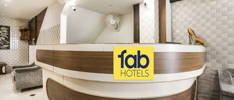 A reception area with a modern design, featuring a wooden reception desk and a sign that reads "fab HOTELS".