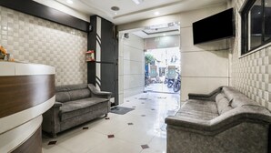 A modern lobby with a reception desk, two sofas, a ceiling fan, and a TV mounted on the wall. - FabHotel SK (Rajkot)