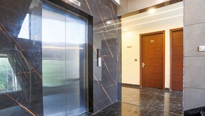 A modern elevator with a glass panel and a marble wall with a geometric pattern. - FabHotel Embrace (New Delhi)