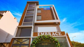 A modern hotel with a prominent 'EMBRACE' sign, a wooden facade, and a welcoming floral arch. - FabHotel Embrace (New Delhi)