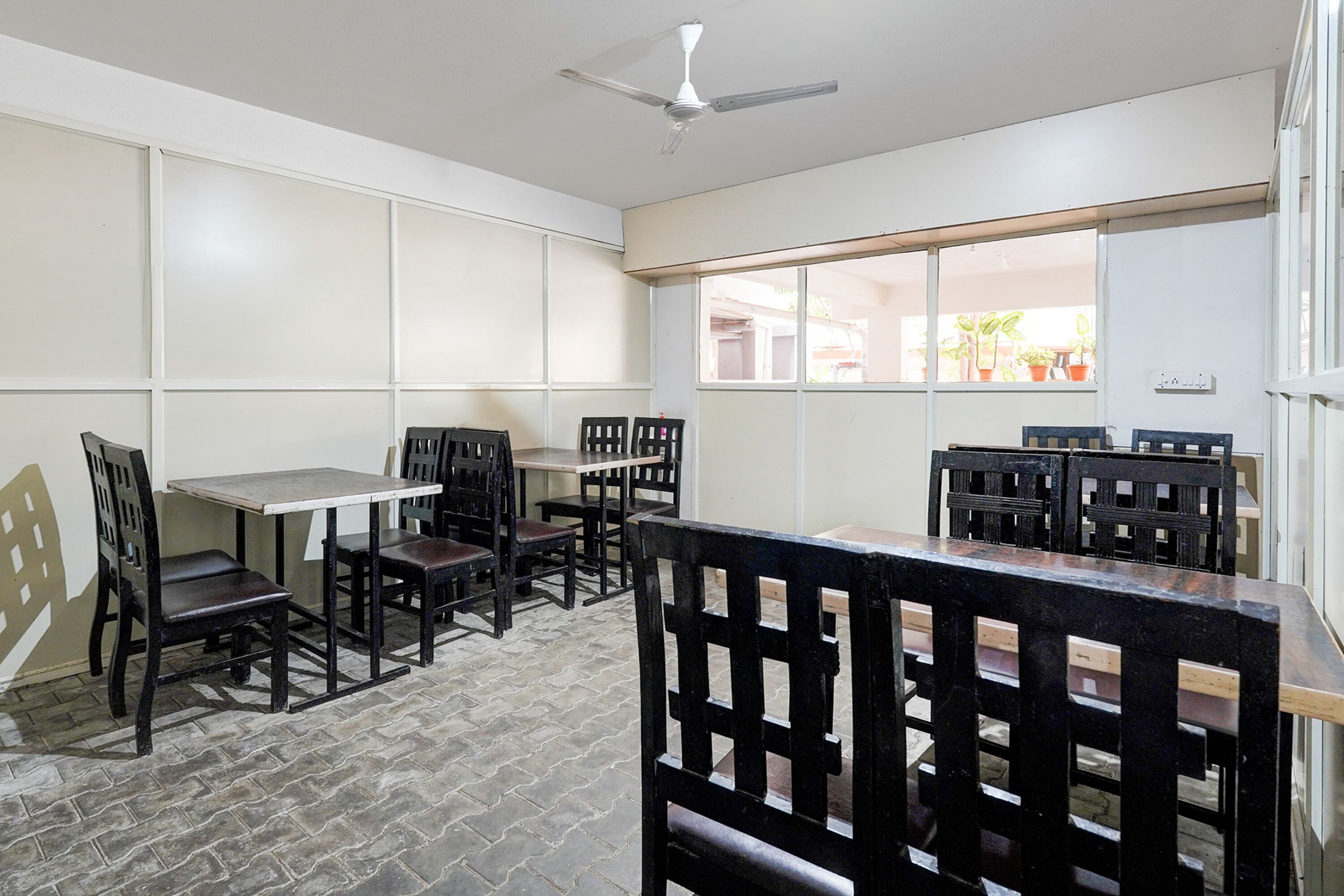 A dining area with tables and chairs, a ceiling fan, and a view of the outside through large windows.