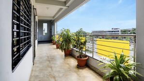 A balcony with potted plants, a yellow railing, and a view of buildings in the distance.