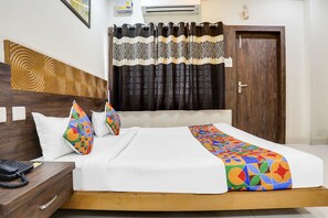 A hotel room with a wooden headboard, a bed with white bedding and colorful geometric pillows, a bedside telephone, and a curtain with a black and white pattern. - FabHotel Blue Star (Nagpur)