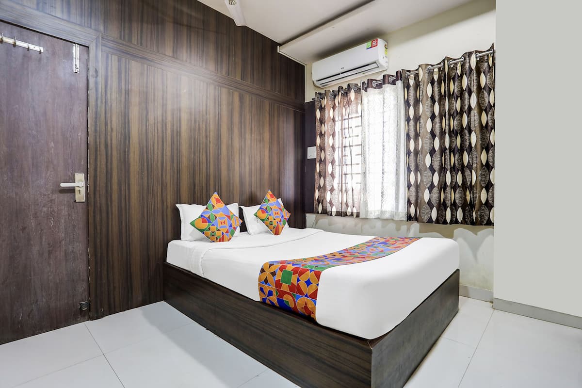 A bedroom with a wooden wardrobe, a bed with a colorful bedspread, and a window with patterned curtains.