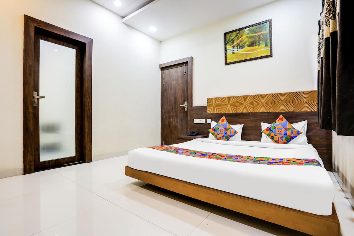 A hotel room with a large bed, a wooden headboard, a framed picture on the wall, and a door with a frosted glass panel.