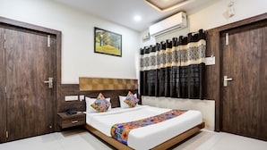 A hotel room with a large bed, wooden wardrobe, and a painting on the wall.