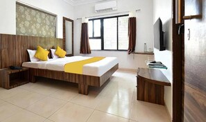 A hotel room with a wooden bed, a bedside table, a desk, and a TV.