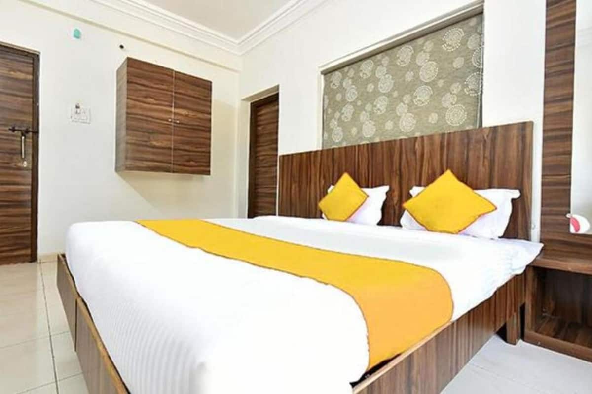Quarto de hotel com uma cama grande, cabeceira de madeira e uma janela com cortinas estampadas.