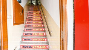 A staircase with red steps and white walls, leading to a room with a wooden door and a small window. - FabExpress Skylark (Chandigarh)