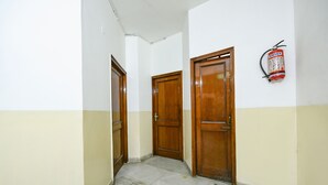 A hallway with two wooden doors, a fire extinguisher on the wall, and a tiled floor. - FabExpress Skylark (Chandigarh)