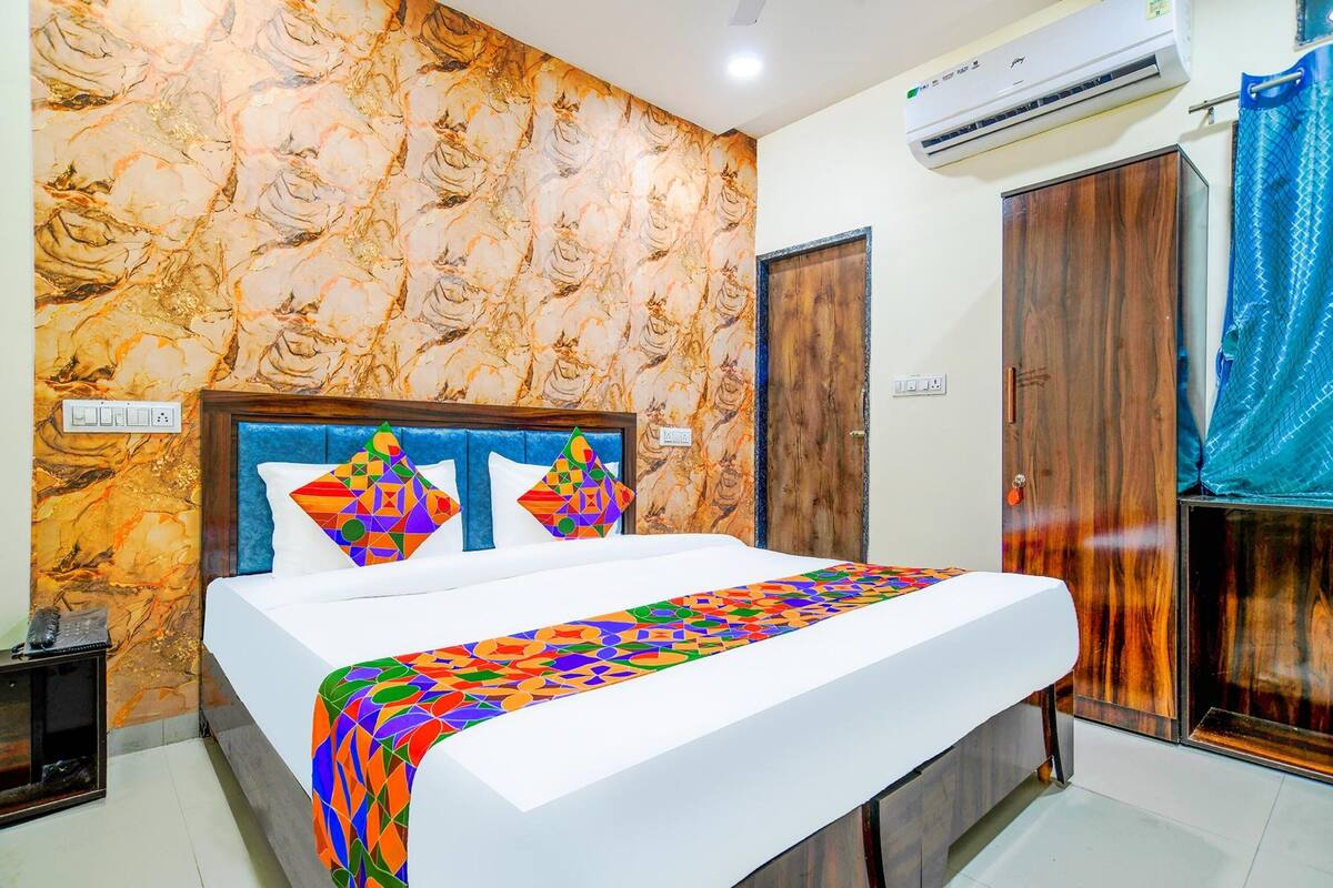 Un dormitorio con papel tapiz estampado, una cama con manta geométrica colorida, un armario de madera y una cortina azul.