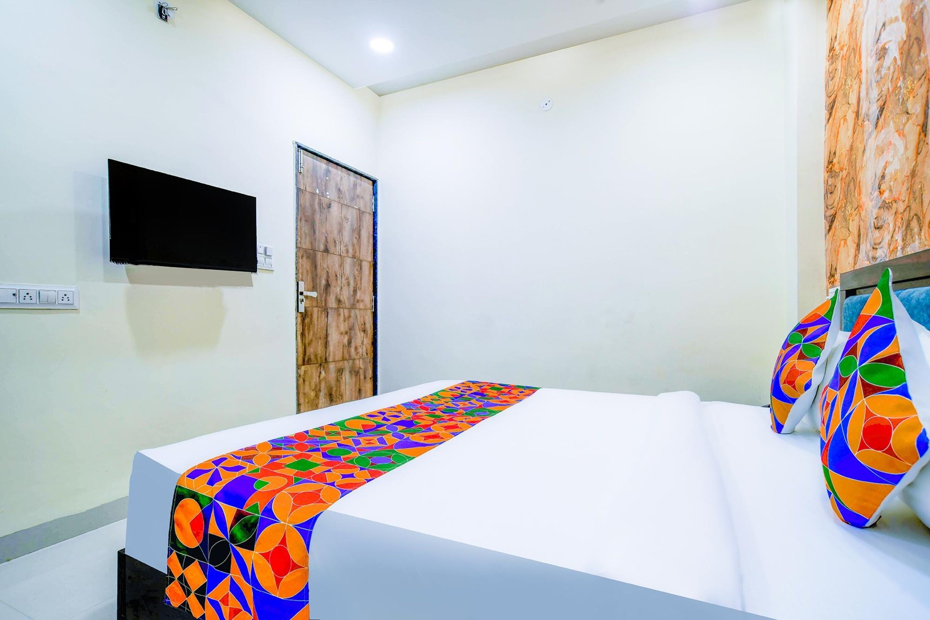 A hotel room with a bed, a flat-screen TV mounted on the wall, and a wooden door.
