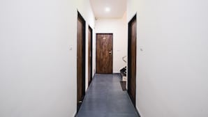 A narrow hallway with a wooden door at the end, white walls, and a black-tiled floor. - FabHotel Ritik (Indore)