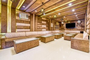A modern lounge area with a long sofa, multiple ottomans, and a flat-screen TV mounted on a brick wall. - FabHotel Log Inn (Jammu)