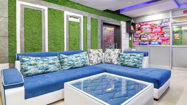 A modern waiting area with a blue sofa set, a glass coffee table, and a green artificial grass wall. - FabHotel Star Lotus (Ranchi)