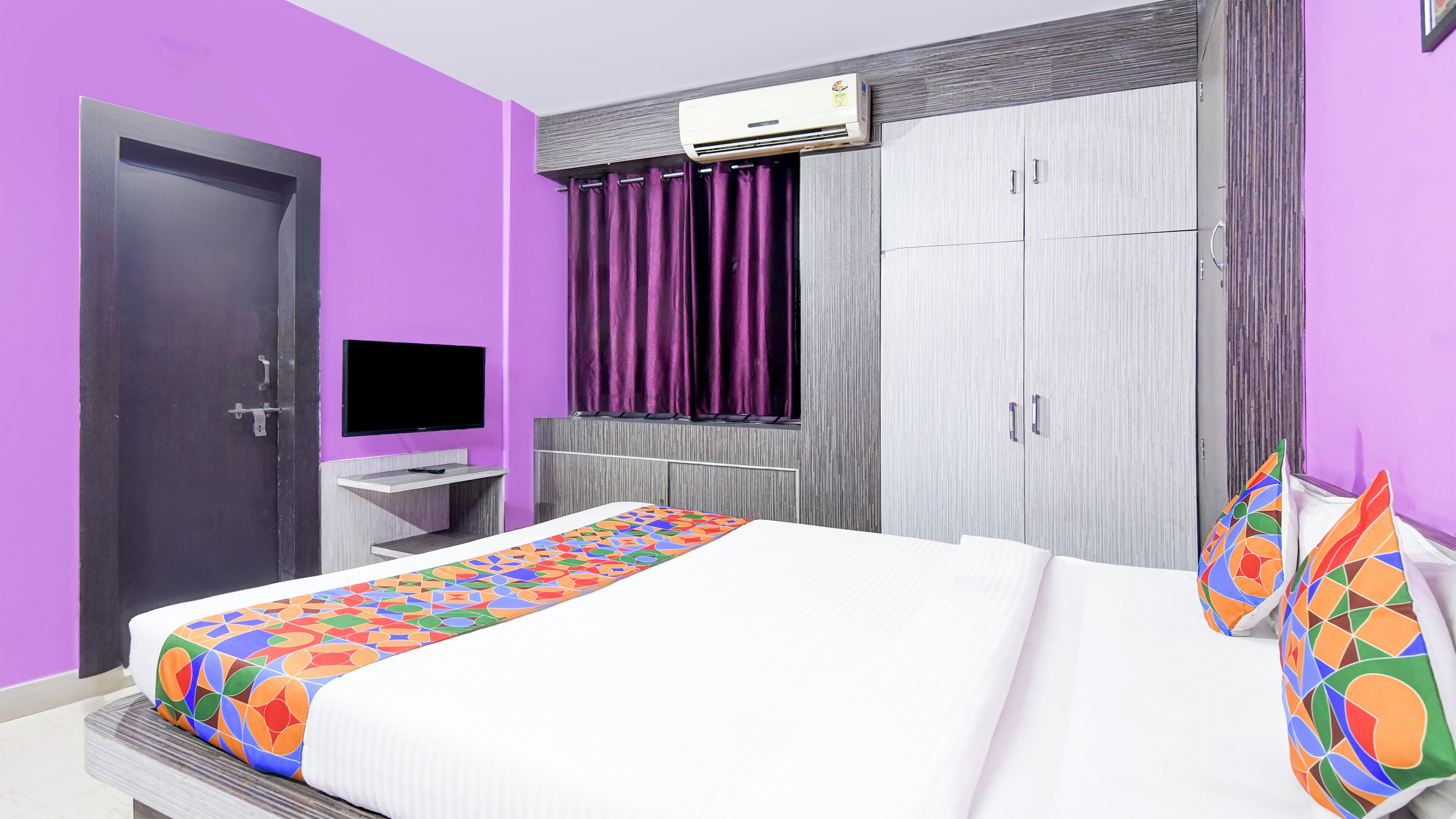 A bedroom with a bed, a TV, a wardrobe, and an air conditioning unit.