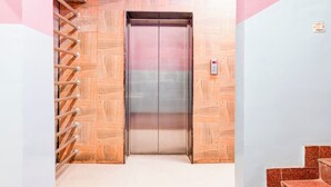 An elevator with a metallic interior, flanked by wooden panel walls and a metal handrail on the left. - FabHotel Star Lotus (Ranchi)