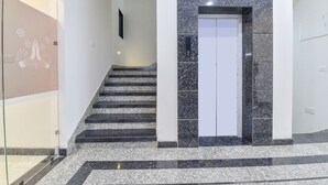 Una escalera que lleva a un ascensor en un edificio moderno con detalles de mármol y un muro decorativo a la izquierda.
