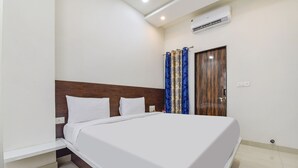 Una cama bien hecha con sábanas blancas, cabecera de madera y cortina azul estampada.