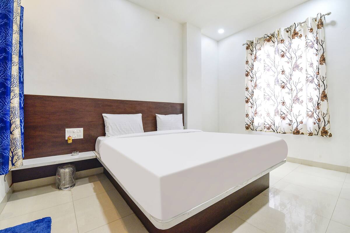 A neatly made bed with white bedding, a wooden headboard, and a small trash bin beside it.