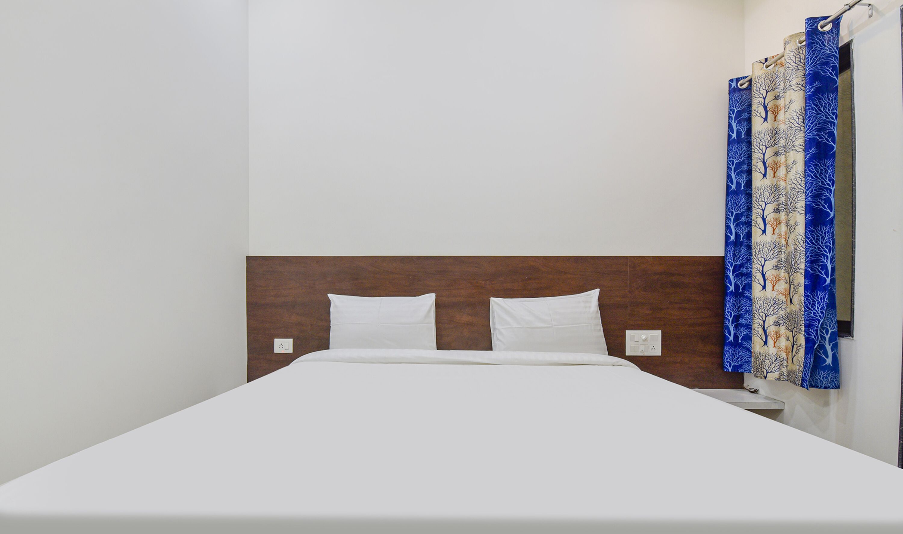 A single bed with white bedding and a wooden headboard in a room with plain white walls.
